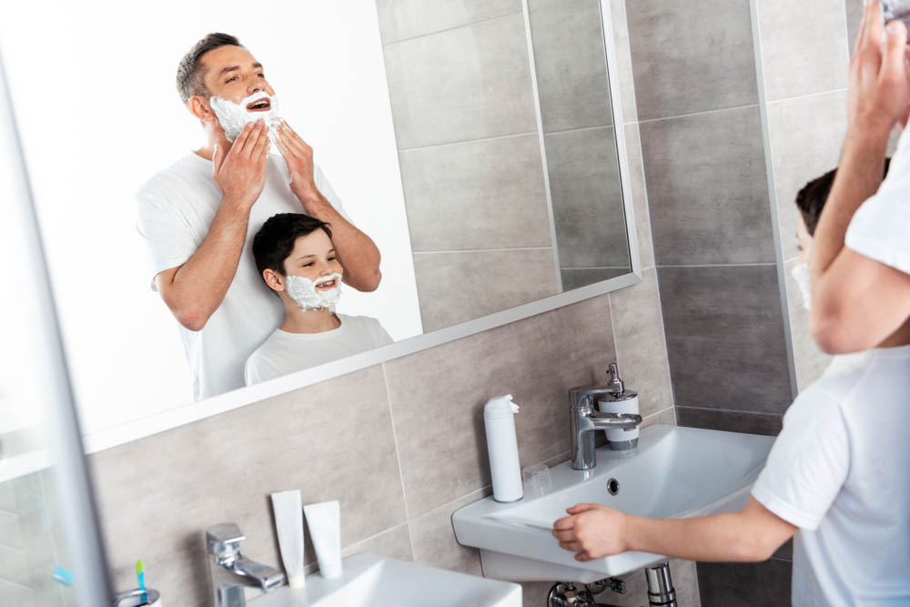 son and father with shaving cream on faces in bathroom
