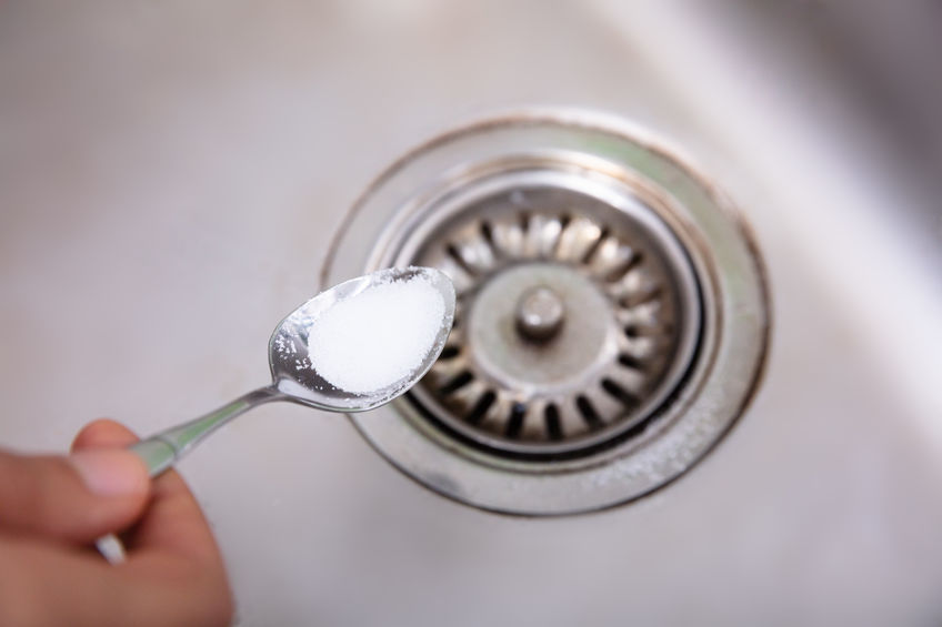A Person Putting The Baking Soda With Spoon On Drain In The Washbasin
