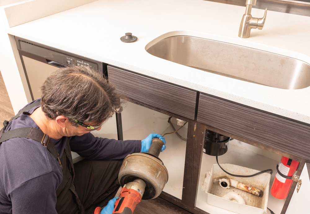 Plumber using an electric hand snake to unclog a kitchen sink