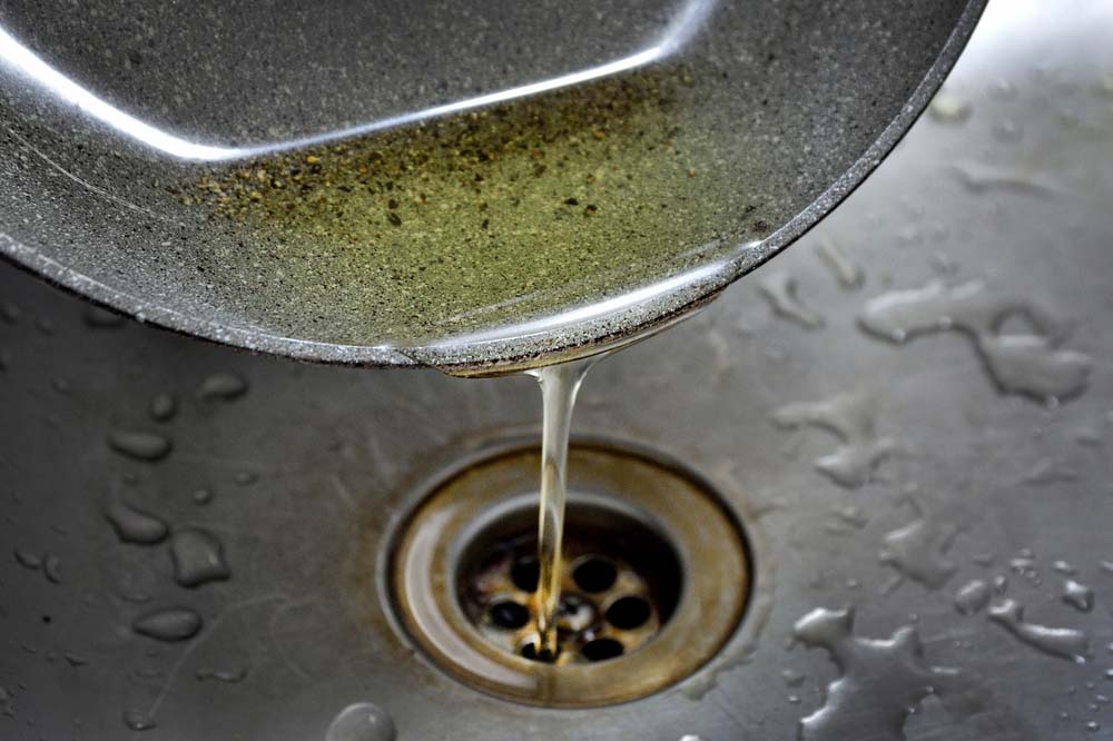 hand pouring grease/cooking oil in a kitchen sink